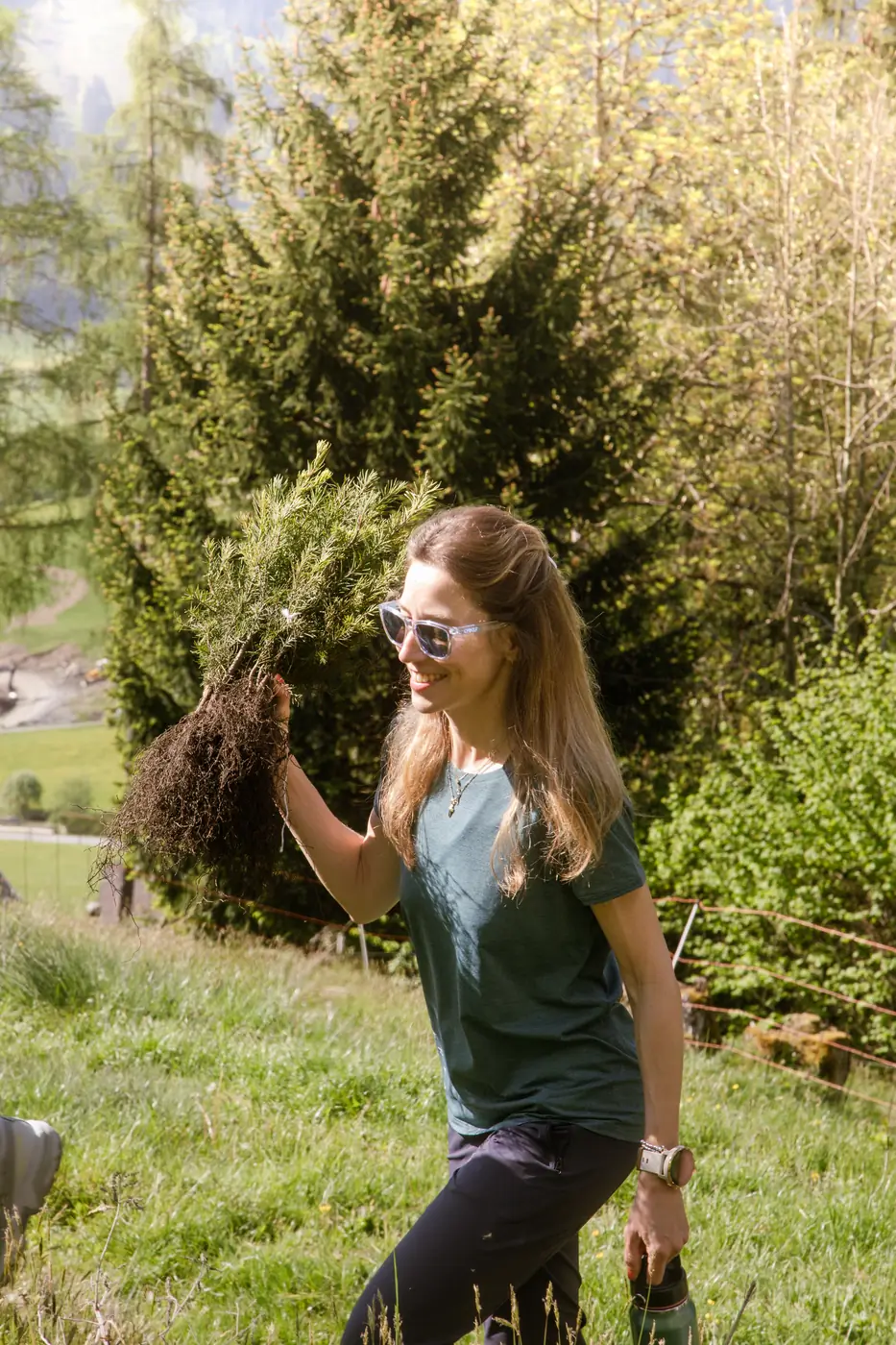 Frau trägt lachend einen Setzling über eine Wiese